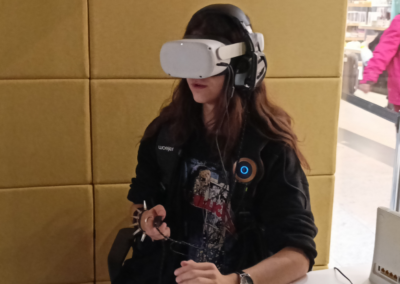 Nastolatka w VR meta na głowie i w kamizelce haptycznej, z kontrolerem w ręce. Ubrana w koszulkę heavy metalową i branzoletę z ćwiekami