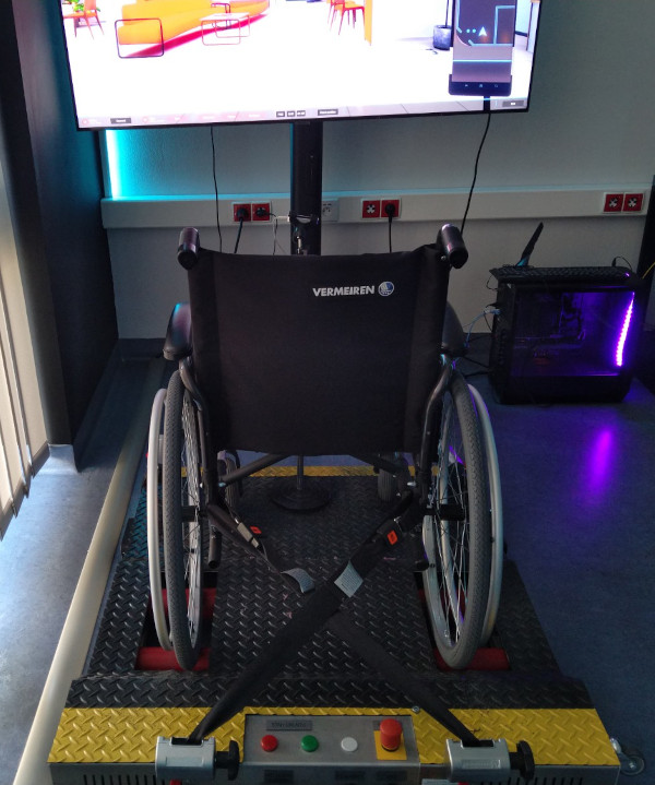 symulator wózka inwalidzkiego. Wózek na specjalnym podwyższaniu, który jeździ w miejscu. Przed nim gra wyświetlona na wielkim telewizorze, w której poruszmy się właśnie za pomocą wózka. 