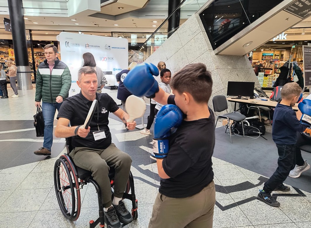 Chłopiec trenuje boks z trenerem na wózku.
